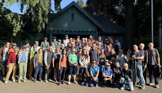 Large group of people, many smiling, looking at the camera while standing in front of a building at Laurelhurst Park.