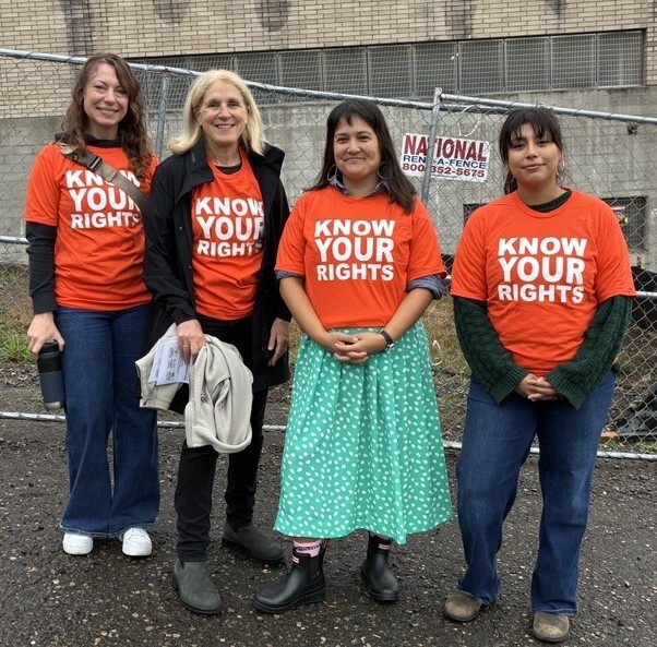 Two PIRC staff members and Julia Brim-Edwards and Tiffany Koyama Lane, all standing in orange shirts that read Know Your Rights, smiling at the camera