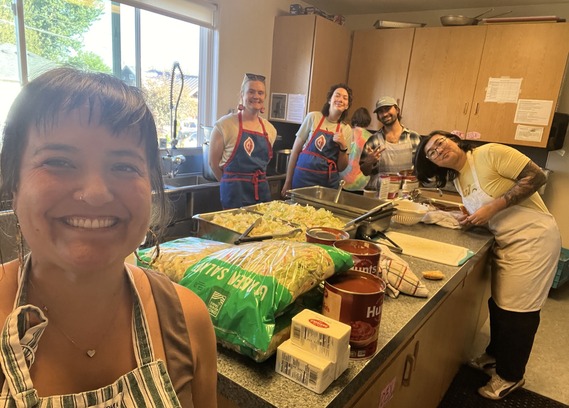 Councilor Koyama Lane and other members of District 3 City Hall staff in aprons, preparing salad and pasta in a kitchen