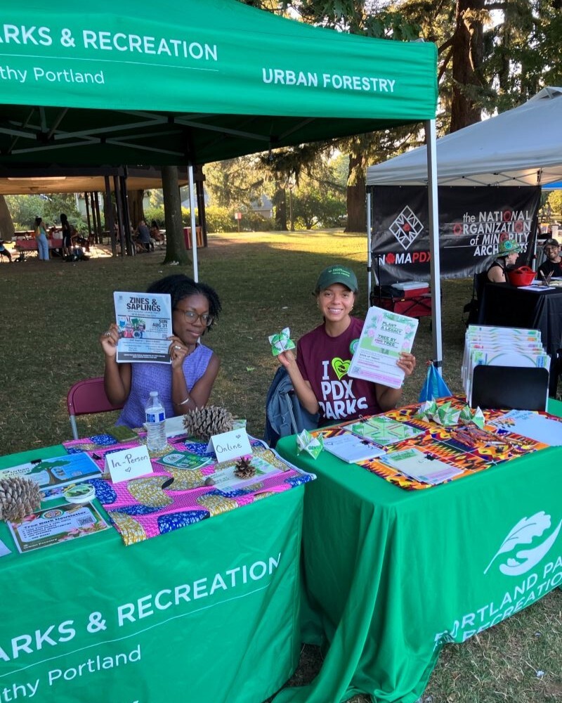 PPR - Two people sitting holding flyers sitting at green table under a green canopy