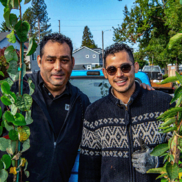Two people smile at the camera, one with a thumbs up, while holding tree saplings