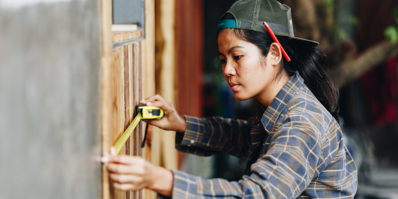 Young construction worker using a tape measure on a wall