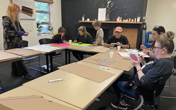 Group of people working at tables arranged in a circle, drawing and writing on posterboards.