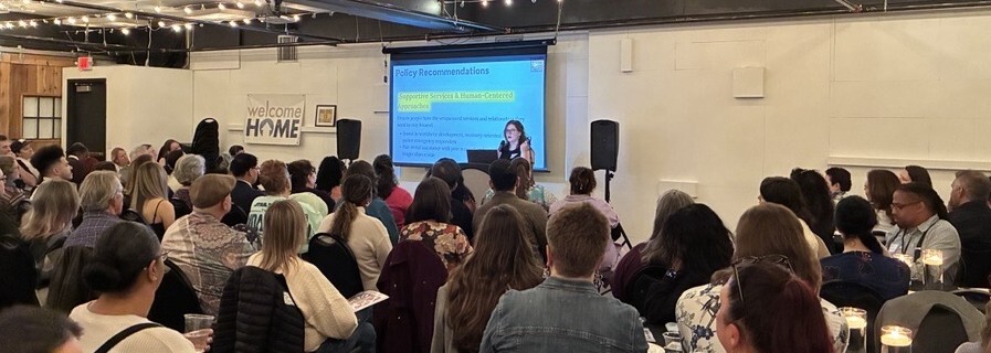 Large group of seated people from the back, watching a presenter using a projector