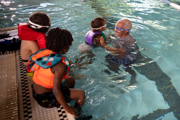 Man wearing goggles helping kids in lifejackets into swimming pool 