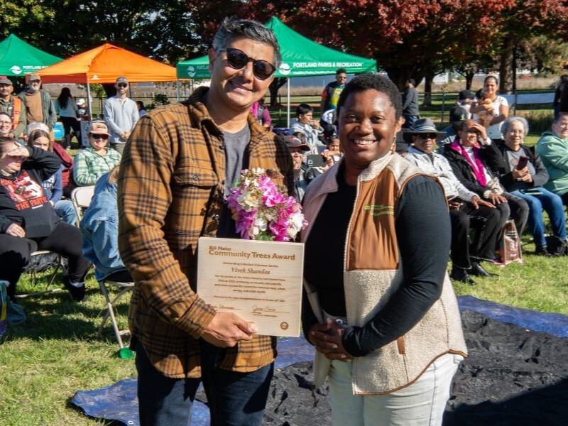 PPR - Two people smiling in front of a seated crowded holding a wooden plaque and flowers 