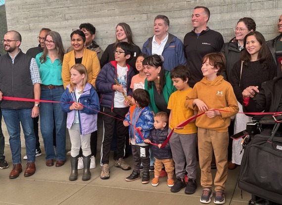 Group of smiling people helping cut a red ribbon