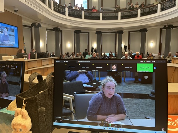 Constituent Lydia Kiesling testifying in front of City Council, with floor and balcony full of people looking on. Photo is taken from the dias