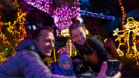 A couple with a young taking a selfie with holiday lighting in the background