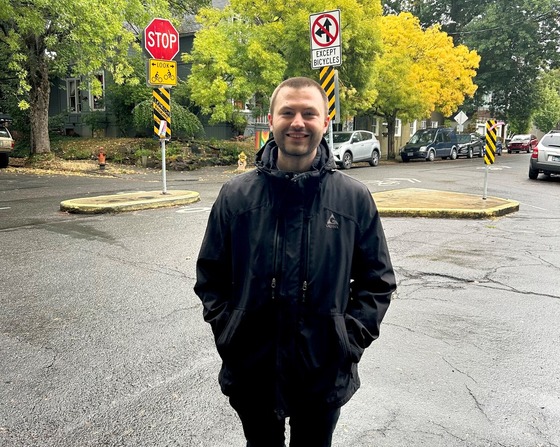 Adult wearing a rain jacket in front of a street intersection. 