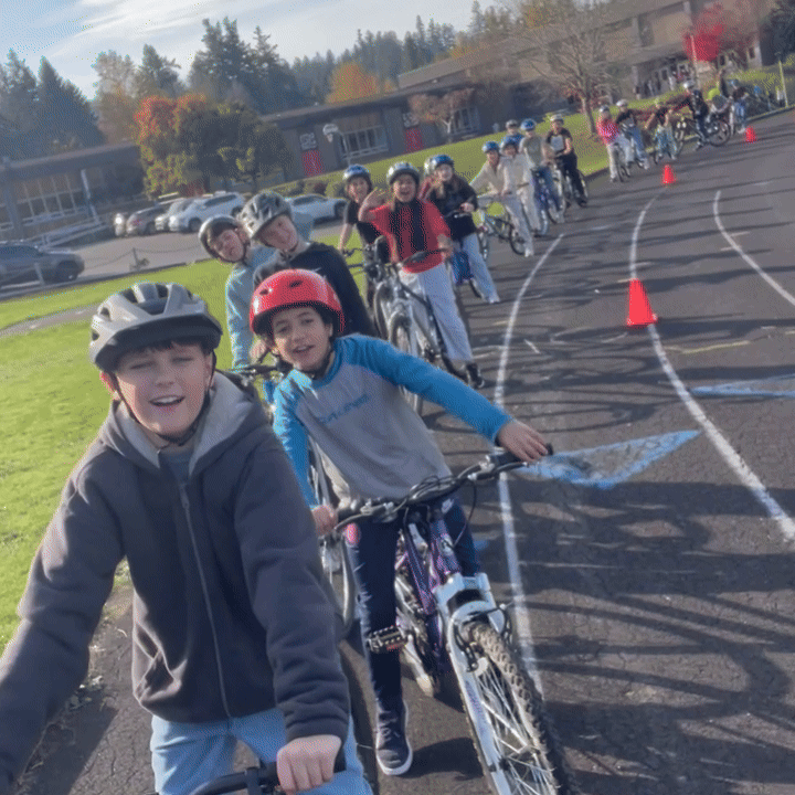 A class of middle school students riding bikes on an outside track.