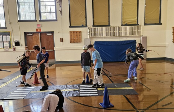 About ten elementary school students practice pedestrian safety on a mock street in a school gym.