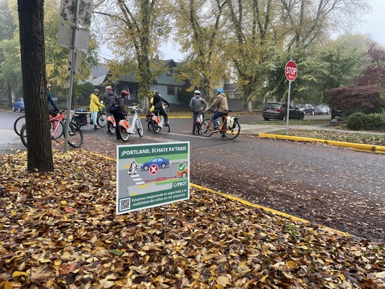 About eight adults on bike stop at an intersection on a fall day. 