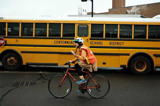 Adult wearing a high visibility safety vest rides a bike past a school bus.