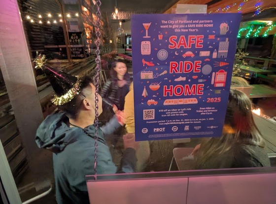 A group of adults celebrate New Year’s Eve with party hats outside a bar with a Safe Ride Home flyer posted inside. 