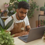 Small business owner surrounded by plants and using a laptop computer
