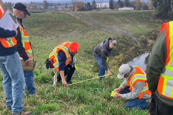 Neighborhood Emergency Team volunteers train in levee inspection - NET - on a grassy slope with water in the background