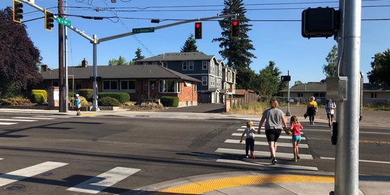 People walking across a street when the pedestrian signal says walk and the traffic light is red for a few seconds before turning green.
