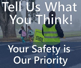 An adult crossing guard helps two children safely walk across a crosswalk and text, "tell us what you think your safety is our priority."