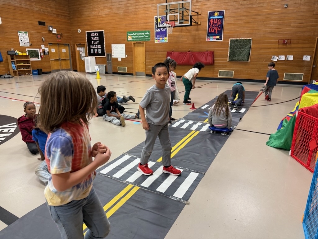 An elementary school class practices how to cross streets safely with a mock street in a school gym.