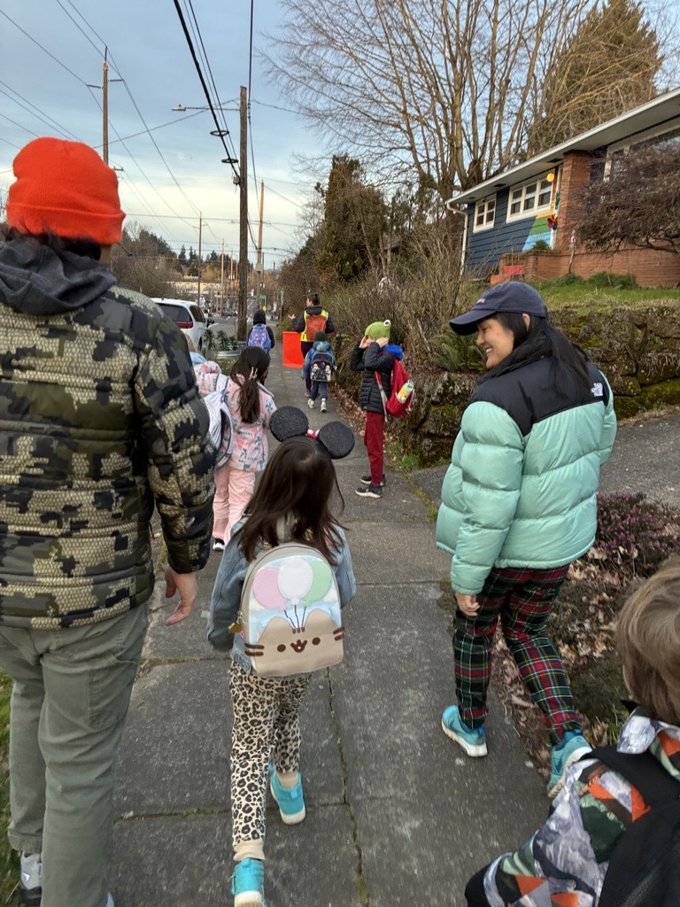 large group of kids and adults walking on sidewalk; Councilor Koyama Lane is looking at child and smiling