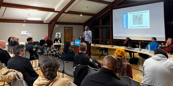 FITCOG community public meeting shows someone speaking at a podium and a room of people listening