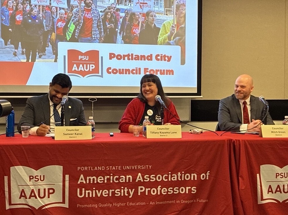 Councilors Kanal, Koyama Lane, and Green sitting in a row behind table with "American Association of University Professors" red tablecloth
