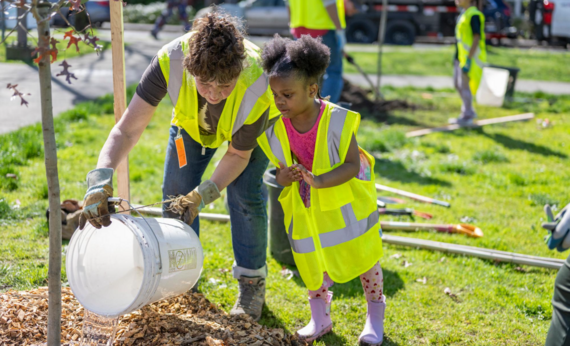 An adult helps a child plant a tree - Urban Forestry tree planting