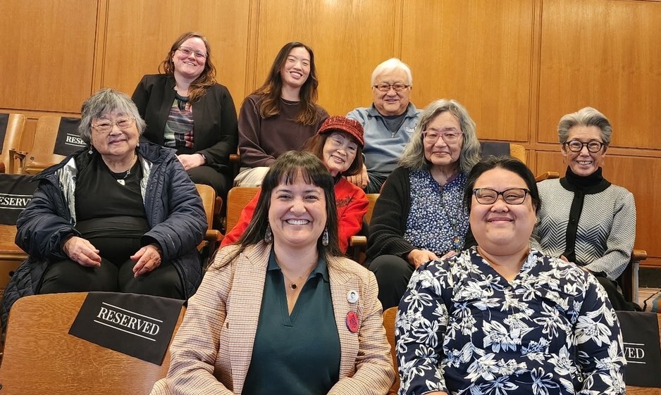 Group of people sitting in wooden chairs, smiling at camera