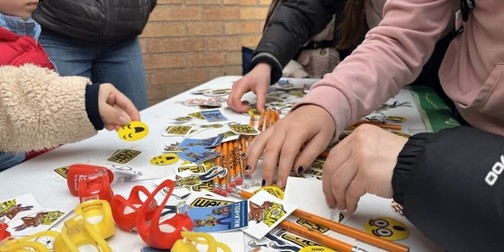 A group of elementary school students grabbing stickers, pencils, and bike lights from a table.