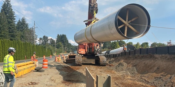 Large water pipe being lowered into the ground by a work crew.