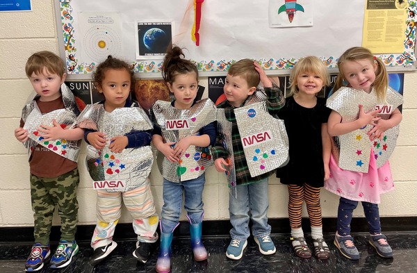 Preschoolers stand in a line dressed as spaceships holding projects they made for a Nasa learning day. 