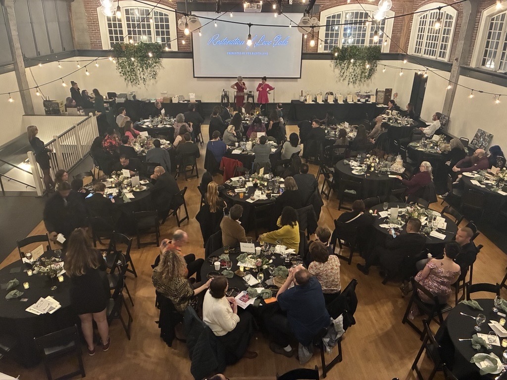 Picture taken from above of room full of tables of people watching two people speak on a stage
