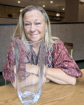 A smiling woman sits with a glass vase award in front of her - Terri is a community center manager