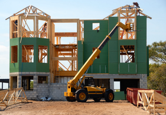 House under construction with heavy equipment on ground and man on roof