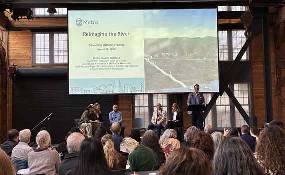Group of people looking at speakers on stage; projector screen reads "Reimagine the River: Councilor Duncan Hwang"