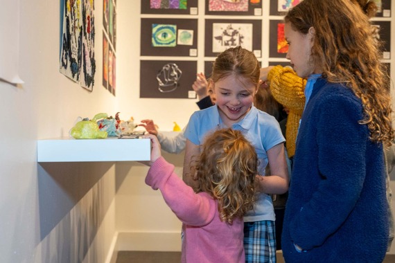 A group of three children looking at an exhibit of children's artwork.