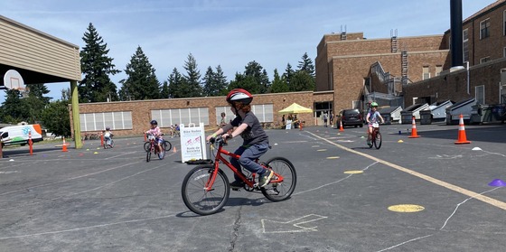 A child practiced riding their red bike on a rodeo course marked in chalk on a school yard black top. 