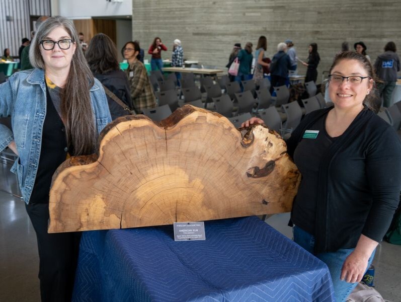 PPR - Two women standing beside a large cut section of a tree on a table