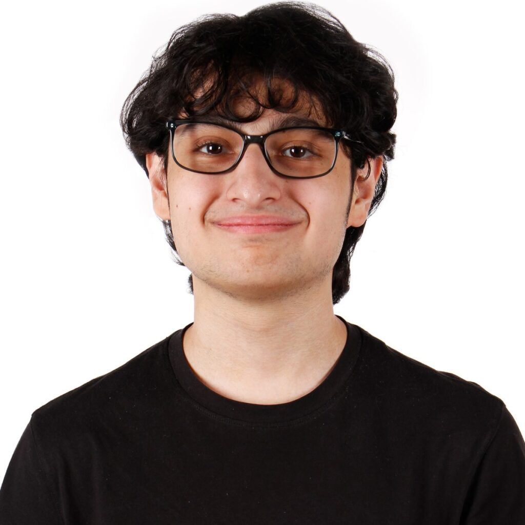 A headshot of a teenager with dark hair and wearing glasses and a black t-shirt. 