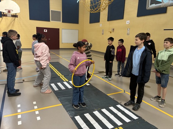 Older elementary school students practice how to use crosswalks on a mock-street in a school gym.