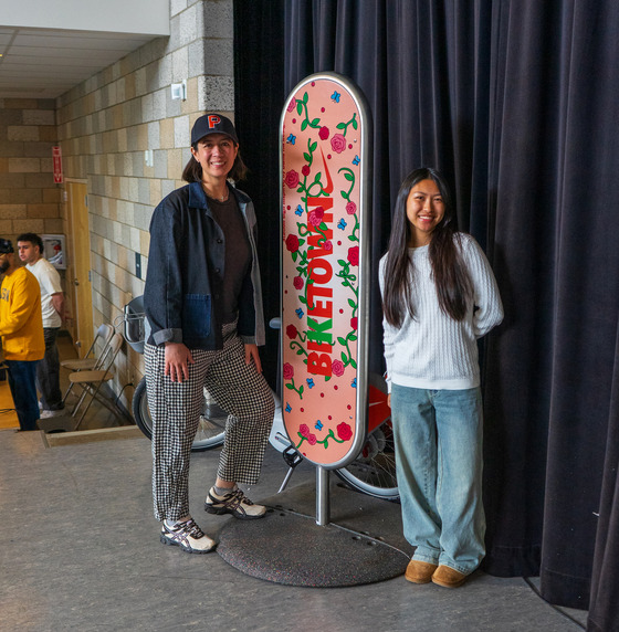A high school student and an adult stand on either side of a BIKETOWK station sign to announce its debut.
