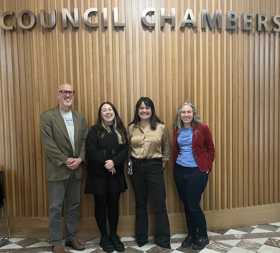 Safe transportation advocates and Councilor Koyama Lane standing in front of wooden wall labeled "Council Chambers"