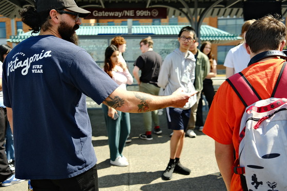 An adult directs teen age students around a transit station as they instruct them on how to use transit.