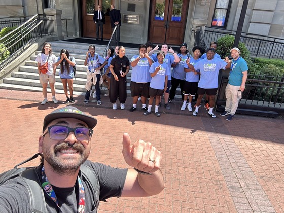 An adult takes a selfie in downtown Portland with a large group of teenagers.