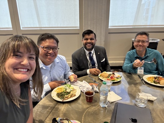 Councilors Koyama Lane (left) and Sameer Kanal (third from left) with Cayle Tern (second from left) seated at a table and smiling
