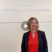 A woman stands in front of a sign that says Portland Permitting and Development - Building Safety Month