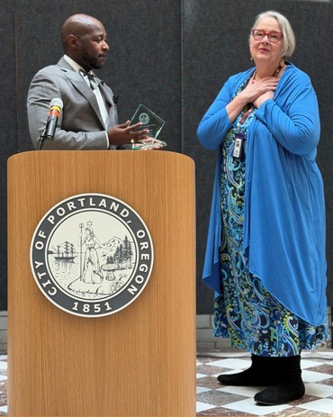 Judith Mowry, who holds her hands over her heart in gratitude, receives an award from Portland City Administrator Raymond Lee.