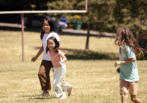 Three campers run and play on a sunny day in the park. 