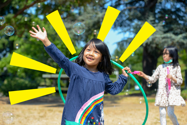 A girl in a park with a hula hoop and sun rays around her head. 
